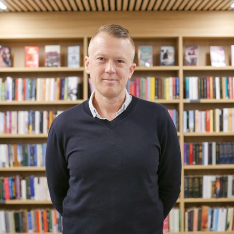 Psykologspesialist Ola Halse Kneppe står smilende inne i et bibliotek. Han ser inn i kameralinsa.