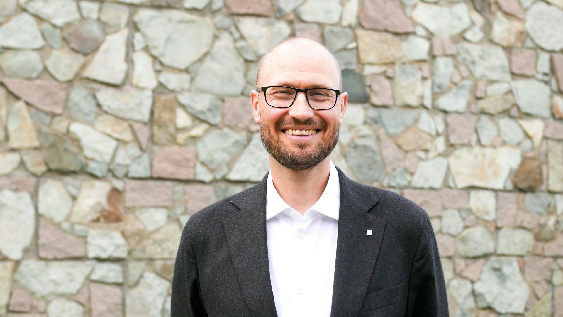 President i Psykologforeningen, Håkon Skard, står smilende foran en bakgrunn av mur.